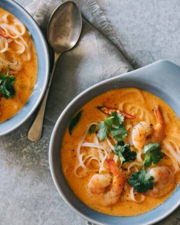 Bowls of spicy red curry and coconut noodle soup with shrimp with a spoon.