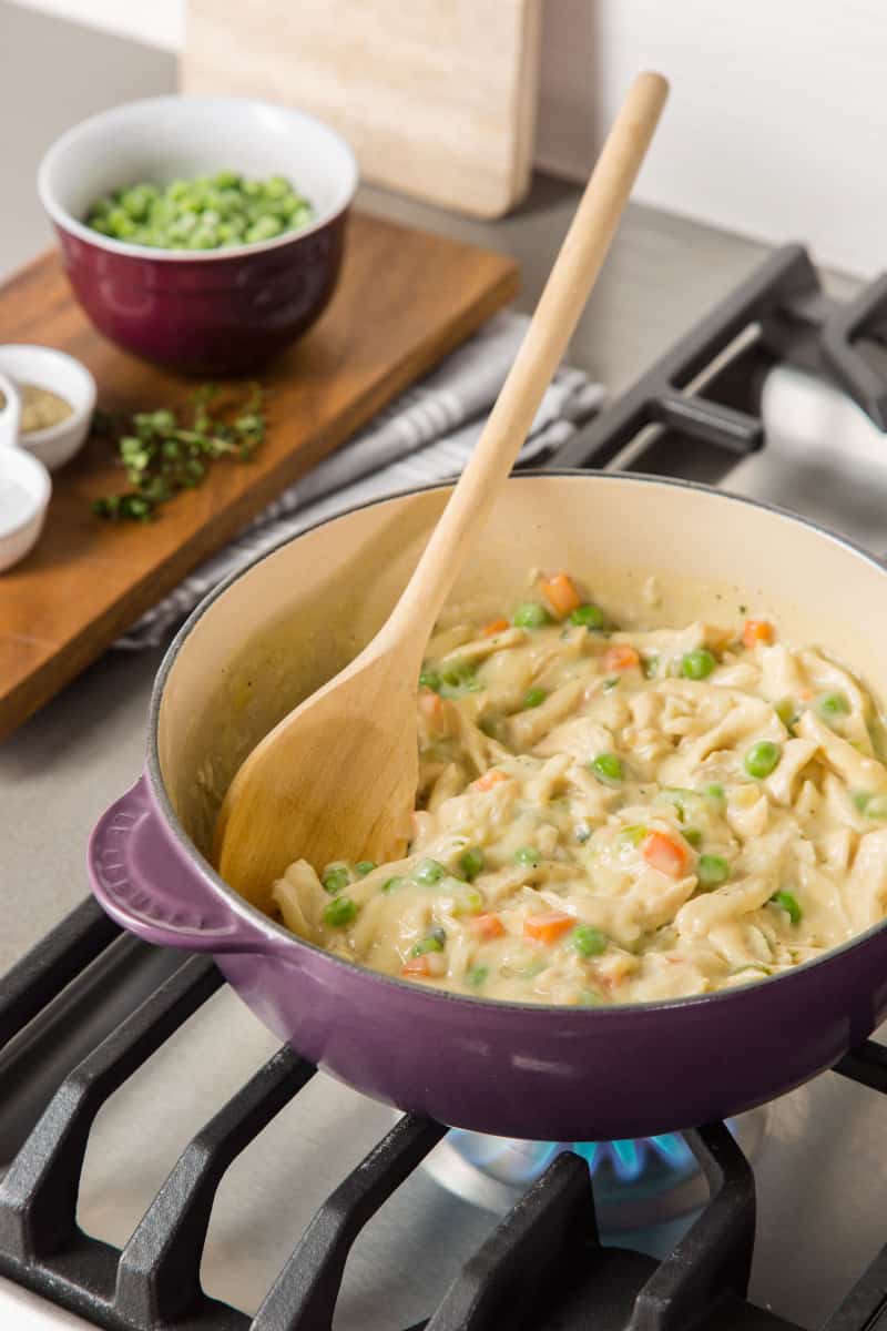A pot of chicken pot pie filling with a wooden spoon. 