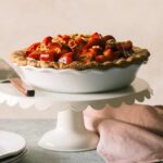 A whole strawberry cream pie on a white cake stand with a pie server.