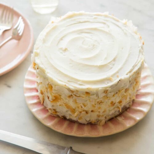 A whole coconut cake next to plates with forks.