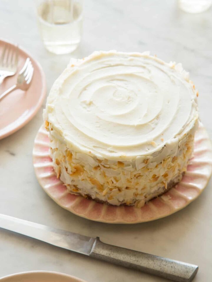 A whole coconut cake next to plates with forks.