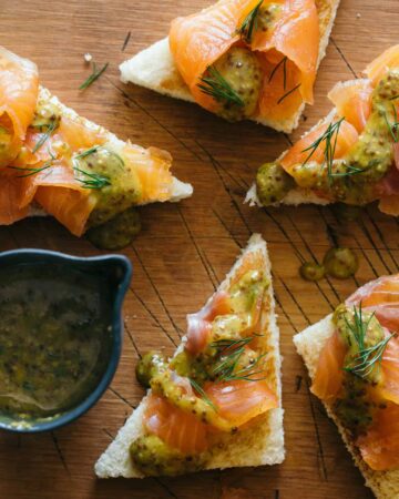 Slices of DIY gravlax with whole grain mustard sauce drizzled and on the side.