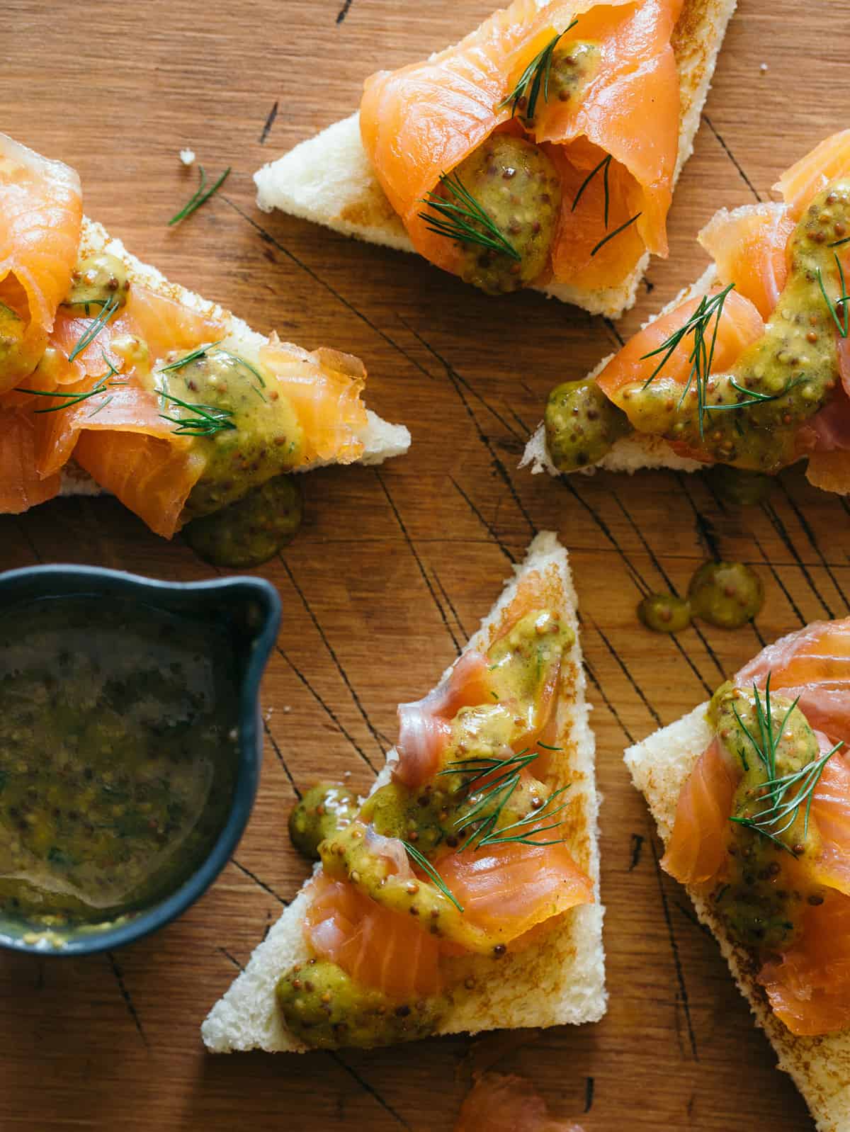Slices of DIY gravlax with whole grain mustard sauce drizzled and on the side.