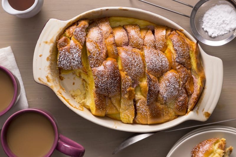 Stacked and stuffed baked French toast with a piece taken out next to coffee.