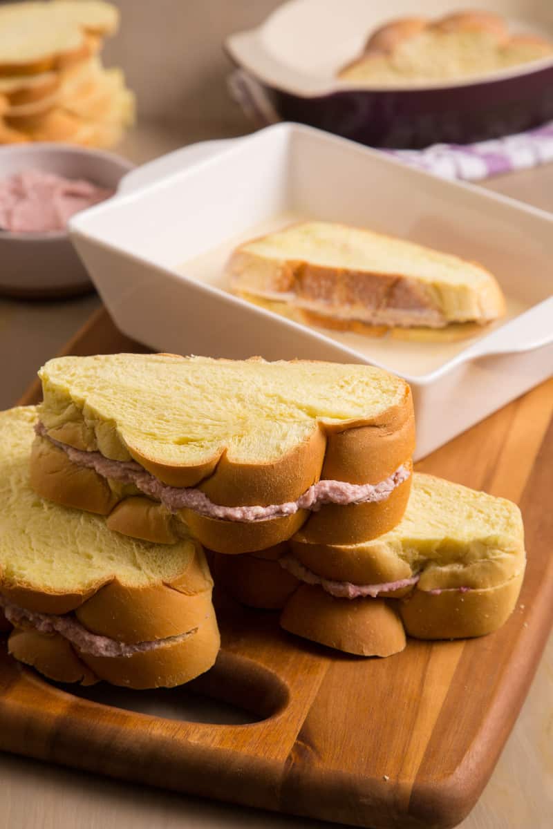 Stuffed French toast with a piece soaking in batter in a shallow dish.