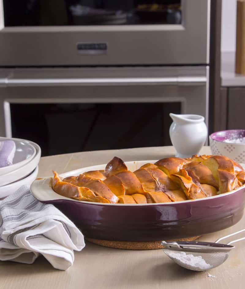 Stacked and stuffed baked French toast in front of an oven, next to plates and linens. 