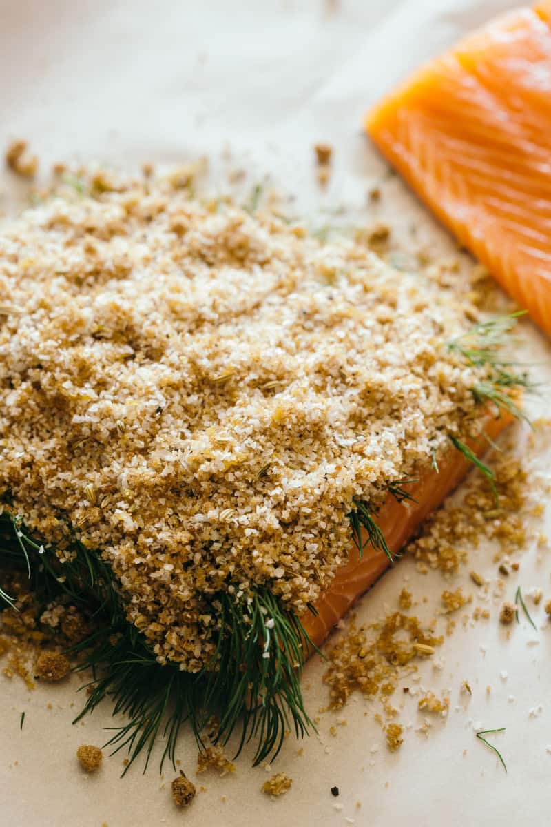 A close up of salmon with cure mixture and dill on top.