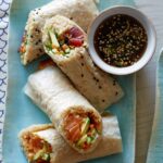 A plate of poke burritos with dipping sauce on the side.