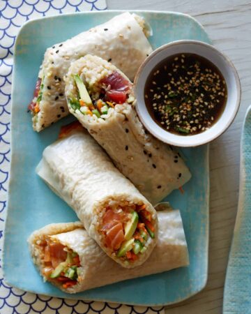 A plate of poke burritos with dipping sauce on the side.