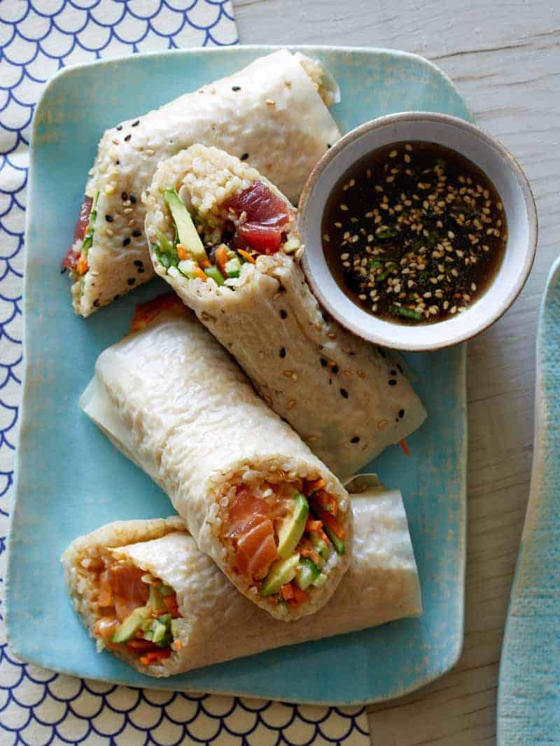 Poke burritos cut in half on a platter with a ramekin of dipping sauce.