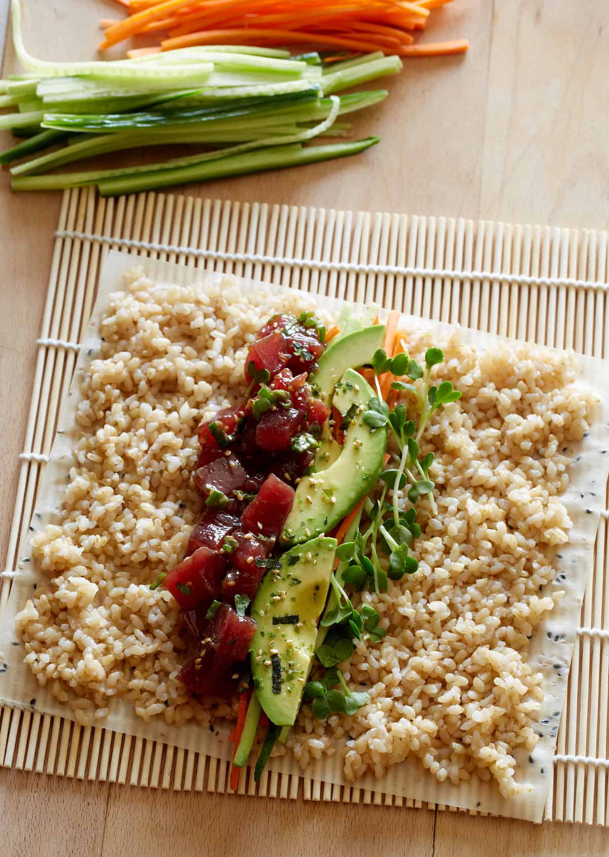 An unrolled poke burrito with ingredients showing layed out on a sushi rolling mat.