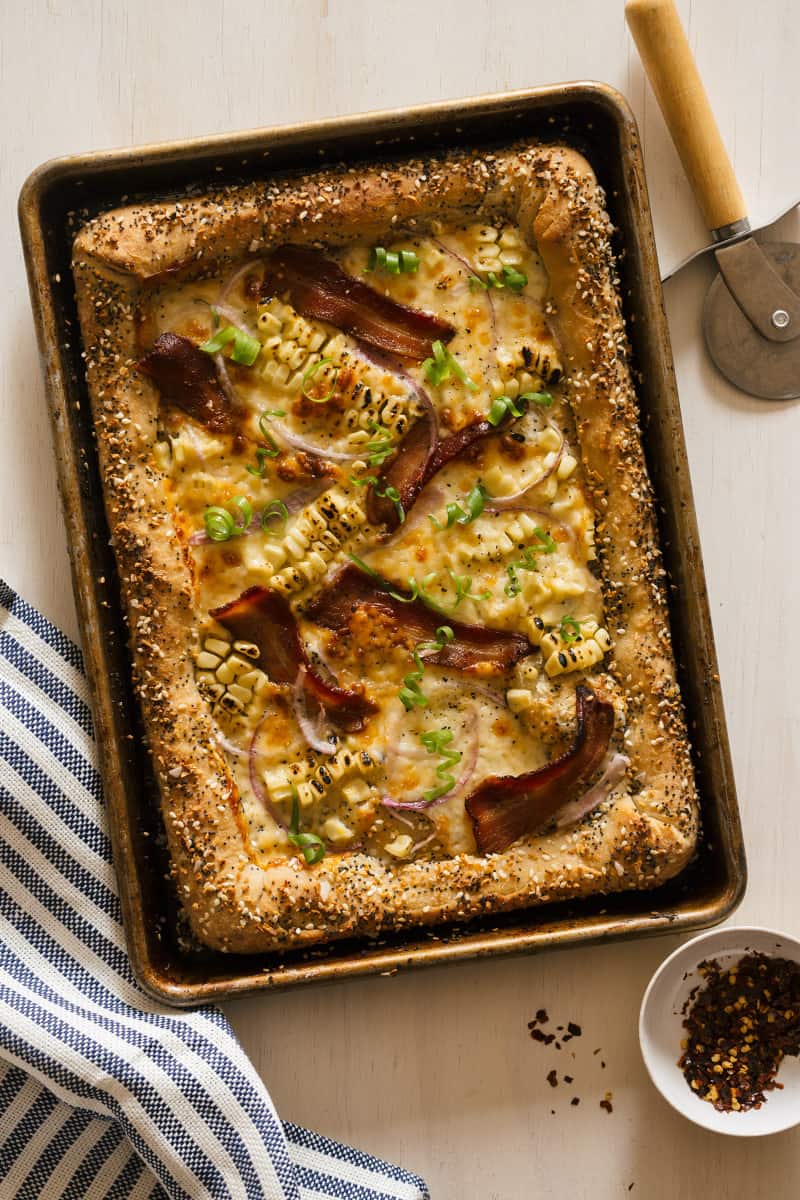 Charred corn and bacon pizza with cream cheese stuffed "everything" crust with a pizza cutter wheel.