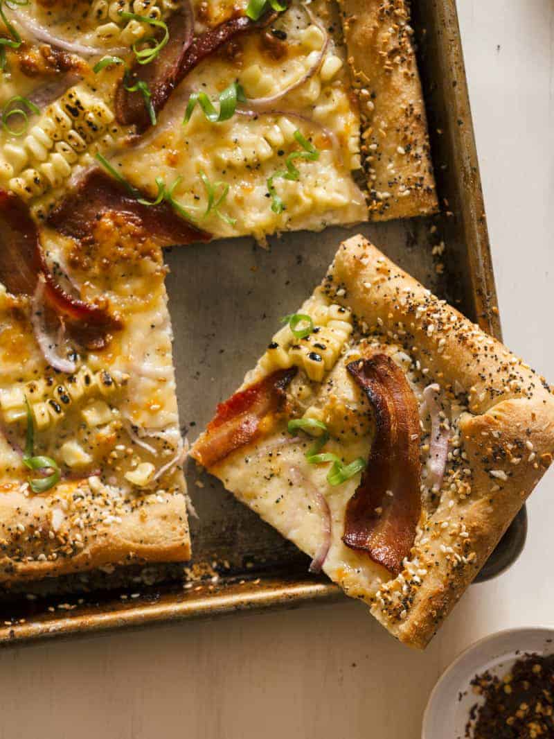 A corner slice of charred corn and bacon pizza with cream cheese stuffed "everything" crust.