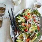 Grilled BLTA gem salad on a platter with serving utensils, plates, and drinks.