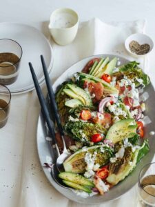 Grilled BLTA gem salad on a platter with serving utensils, plates, and drinks.