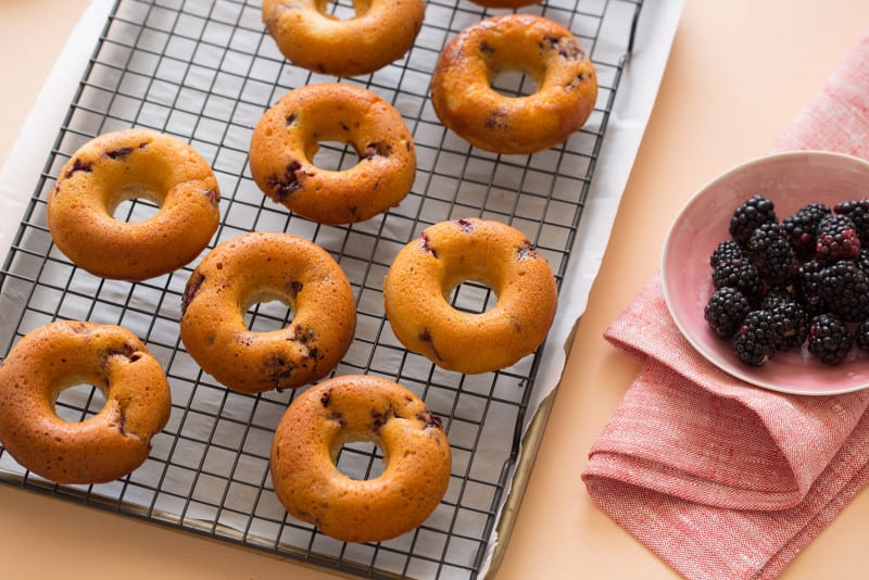 Baked blackberry and cardamom doughnuts on a cooling rack.