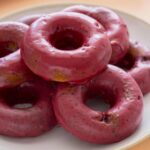 A close up of baked blackberry and cardamom doughnuts stacked on a plate.