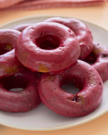 A close up of baked blackberry and cardamom doughnuts stacked on a plate.