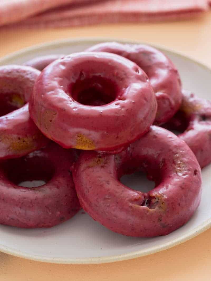 A close up of baked blackberry and cardamom doughnuts stacked on a plate.