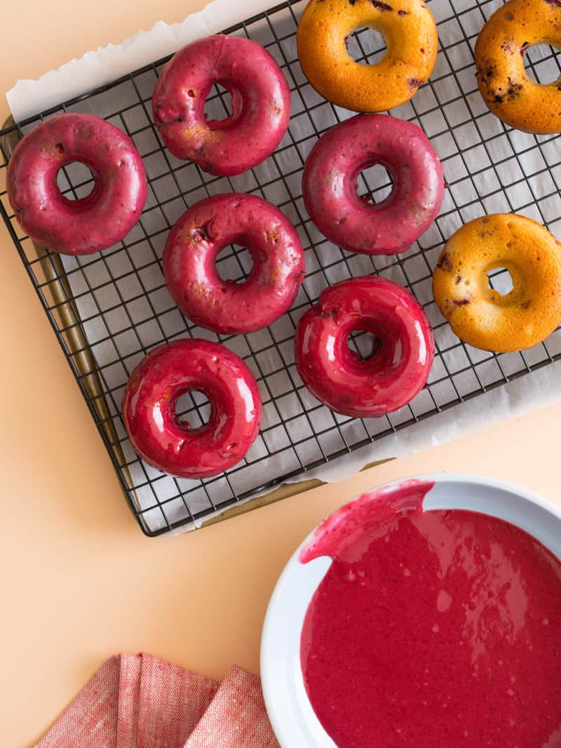 Baked blackberry and cardamom doughnuts being glazed on a rack.