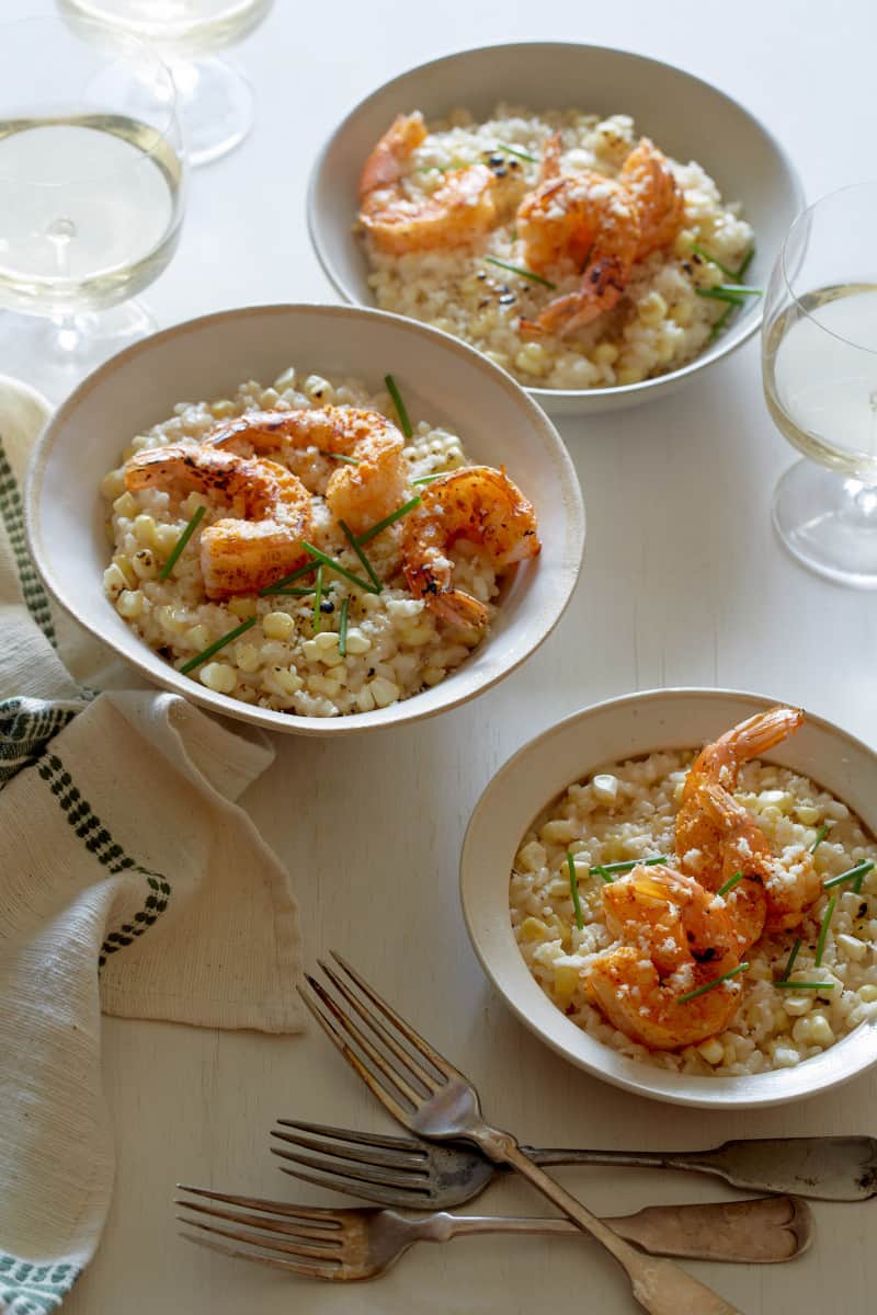 Bowls of sweet corn risotto and Cajun shrimp with forks and drinks.