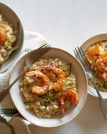 Bowls of sweet corn risotto with Cajun shrimp and forks.
