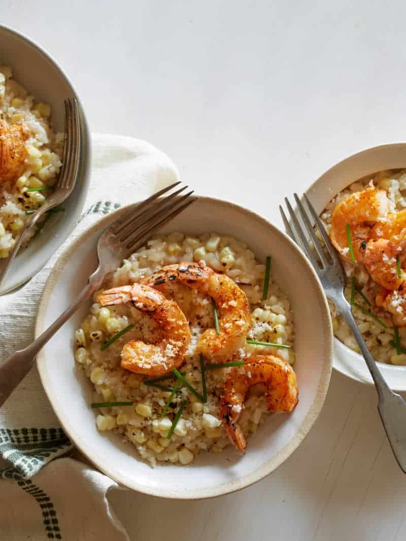 Several bowls of sweet corn risotto with cajun shrimp and forks.