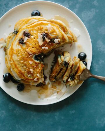 A plate of brown sugar, coconut, blueberry pancakes with a bite on a fork.