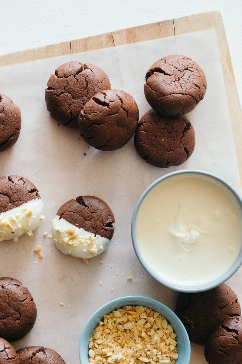 Peanut butter stuffed chocolate cookies being dipped in a bowl of white chocolate.