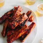 A plate of spicy marinated and grilled spare ribs next to drinks.