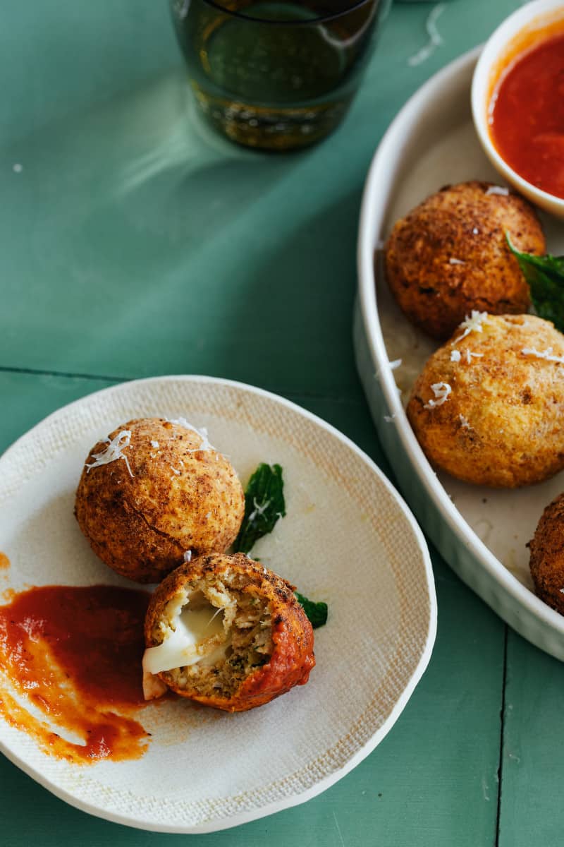 Plates of mozzarella stuffed chicken parmesan meatballs with marinara sauce on the side.