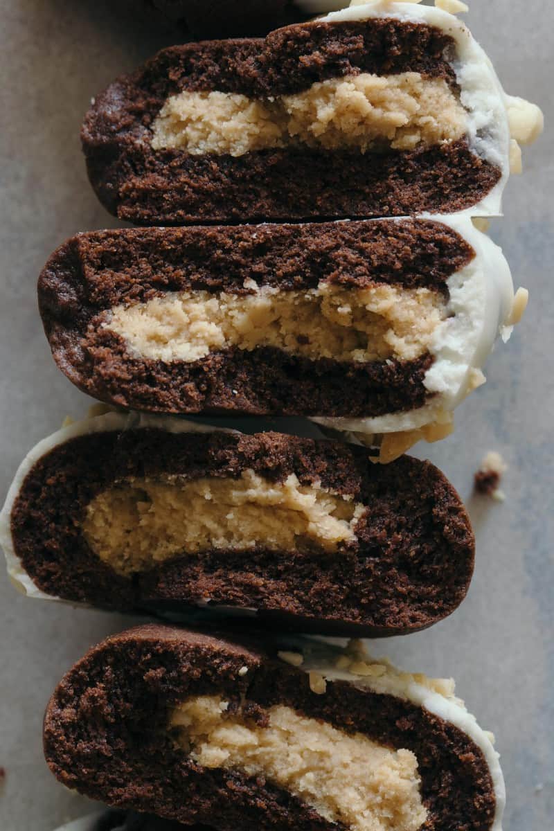A close up of white chocolate dipped, peanut butter stuffed chocolate cookies broken in half.