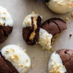 A close up of white chocolate dipped, peanut butter stuffed chocolate cookies, one broken in half.