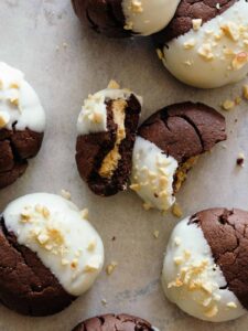 A close up of white chocolate dipped, peanut butter stuffed chocolate cookies, one broken in half.