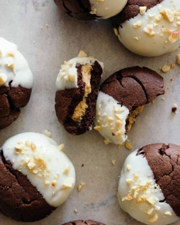 A close up of white chocolate dipped, peanut butter stuffed chocolate cookies, one broken in half.