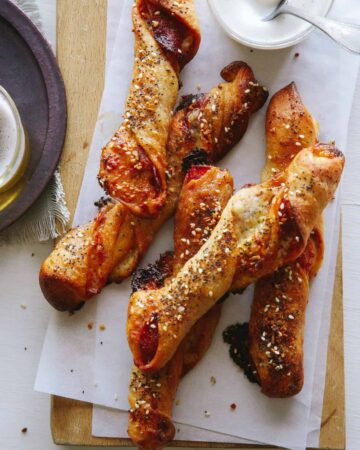 Pizza stuffed breadsticks on a wooden cutting board next to a plate.