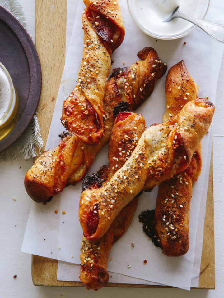 Pizza stuffed breadsticks on a wooden cutting board next to a plate.