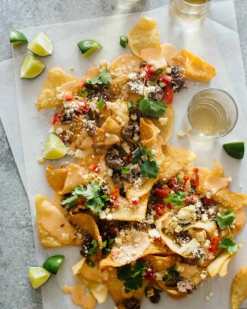 Korean BBQ nachos with lime wedges and a drink.