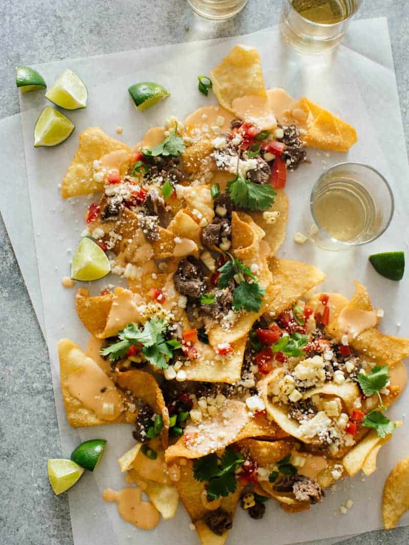 Korean BBQ nachos with lime wedges and a drink for a Super Bowl appetizer. 