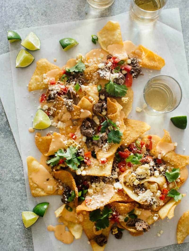 Korean BBQ nachos with lime wedges and a drink.