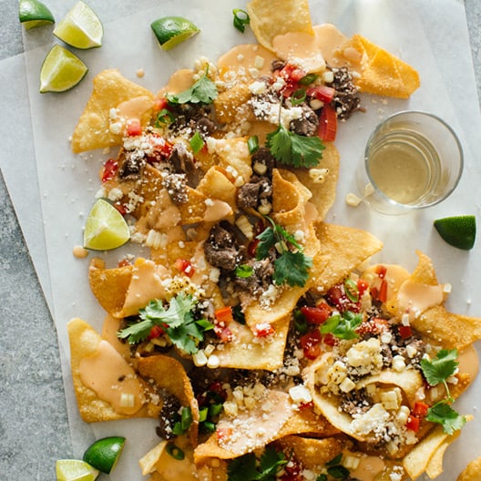 Korean BBQ nachos with lime wedges and a drink.