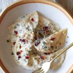 A bowl of butternut squash mezzaluna with roasted garlic sage cream sauce and a fork.