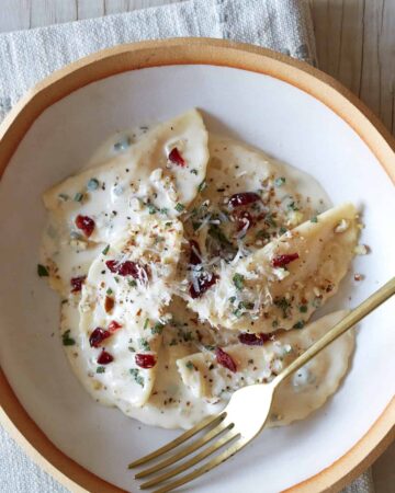 A bowl of butternut squash mezzaluna with roasted garlic sage cream sauce and a fork.