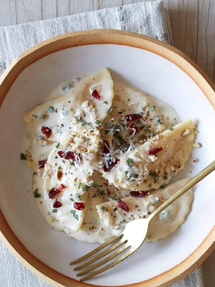 A bowl of butternut squash mezzaluna with roasted garlic sage cream sauce and a fork.