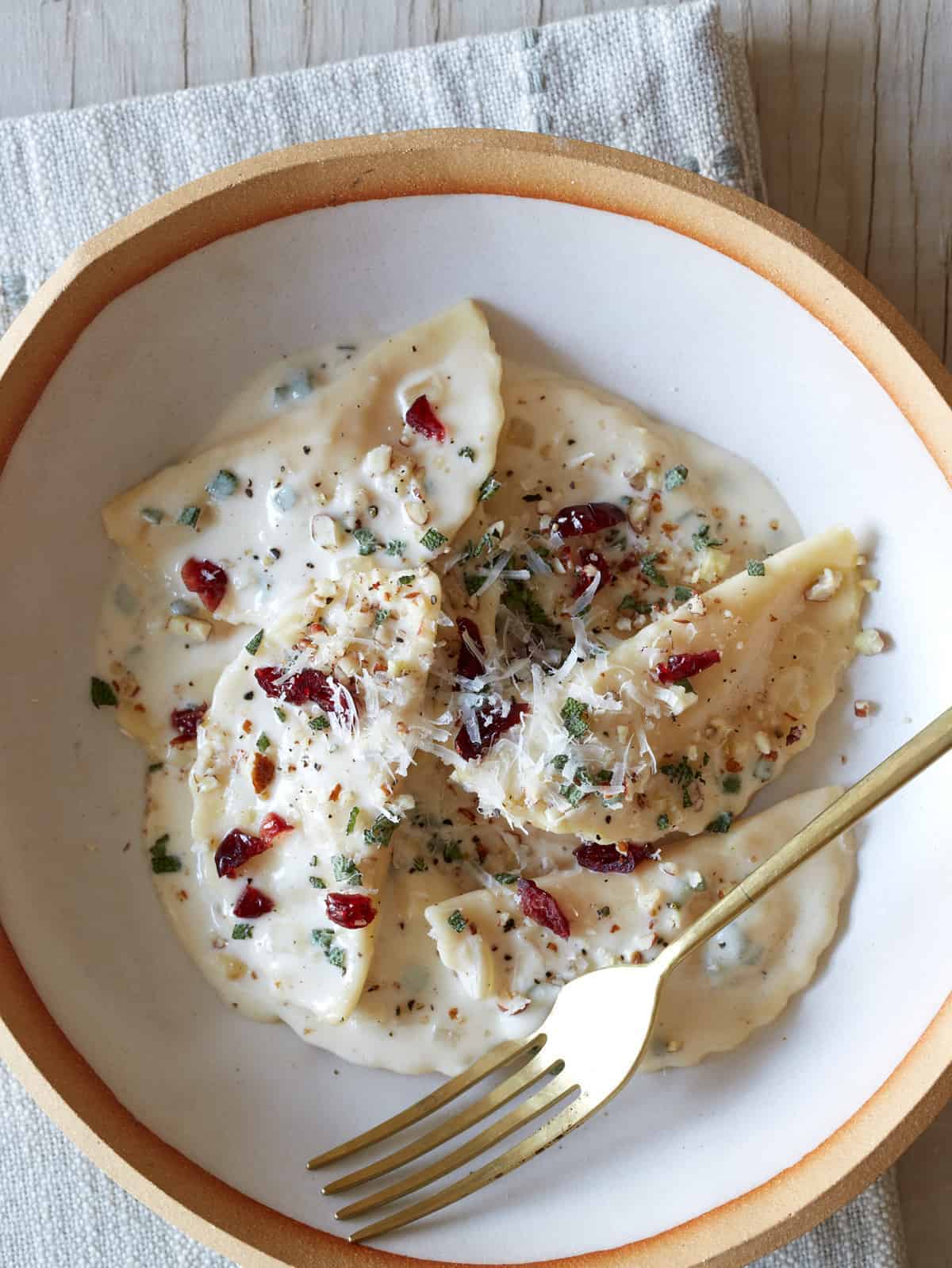 A bowl of butternut squash mezzaluna with roasted garlic sage cream sauce and a fork.