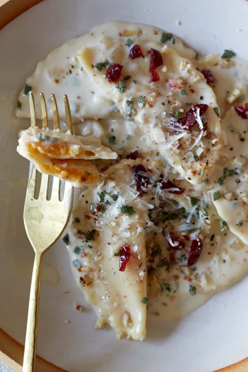 A close up of butternut squash mezzaluna with roasted garlic sage cream sauce on a fork.