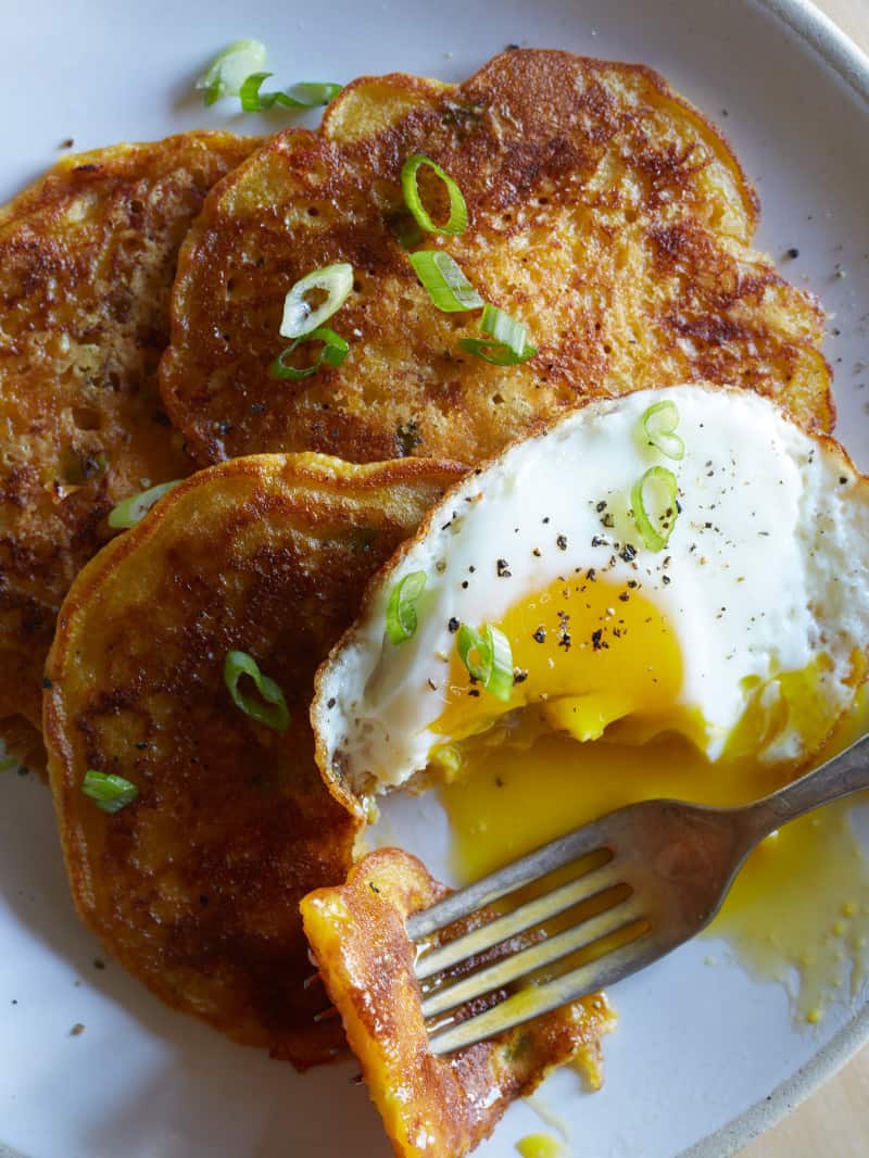 A close up of cheesy pumpkin pancakes with a fried egg, broken yolk, and a fork.