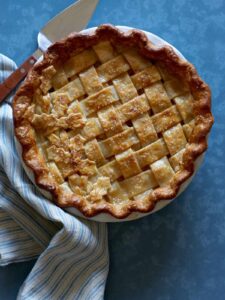 A whole maple, pear, ginger pie with linens and a pie server.