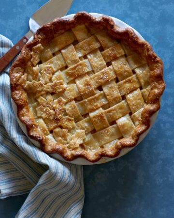 A whole maple, pear, ginger pie with linens and a pie server.