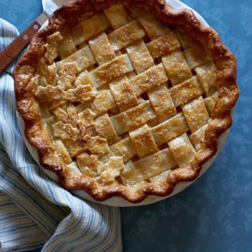 A whole maple, pear, ginger pie with linens and a pie server.